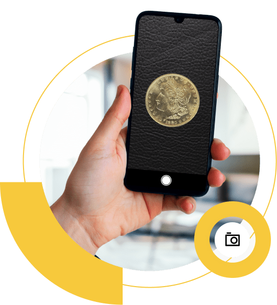 A hand holds a smartphone displaying the image of a vintage gold coin with intricate details against a yellow circular design. A camera icon hints at photography or appraisal use in modern apps.