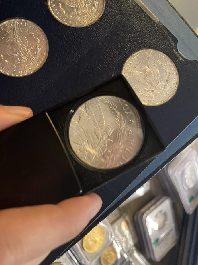 Numismatist inspecting a Morgan Silver Dollar under magnifying glass, focusing on identifying marks and wear for valuation.